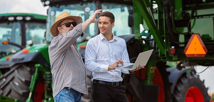 Duas pessoas conversando na fazenda, uma com laptop nos braços.